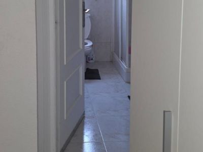 Vista parcial de un baño con suelo de gres claro, inodoro, ventana y ducha con mampara. Azulejos de pared con cenefa decorativa.