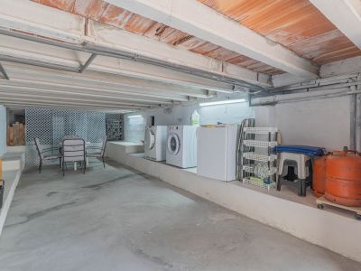 Amplio espacio inferior con zona de lavandería equipada, almacenamiento y un área de estar informal. Destaca su techo con vigas de hormigón y bovedillas cerámicas expuestas.