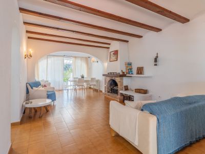 Amplio salón con suelos de terracota, vigas de madera vistas y chimenea de ladrillo. Un arco conecta con el luminoso comedor y la terraza, ofreciendo luz natural.