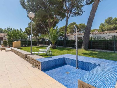 Detalle de la zona de piscina comunitaria con azulejos de mosaico azul, ducha exterior y pavimento claro, enmarcada por césped y vegetación.