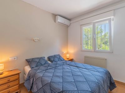 Dormitorio con cama doble, mesitas de noche de madera y aire acondicionado. Ventana con rejas y vistas a la vegetación, además de radiador.
