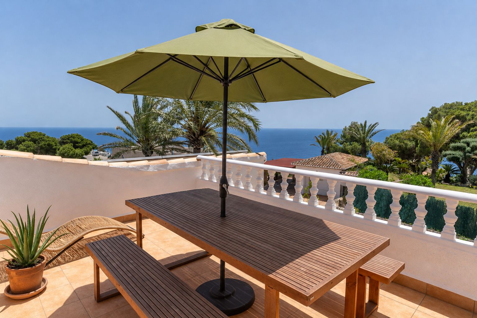 Amplia terraza en la azotea con mesa y bancos de madera, sombrilla verde y vistas panorámicas al mar Mediterráneo, enmarcada por una balaustrada blanca.