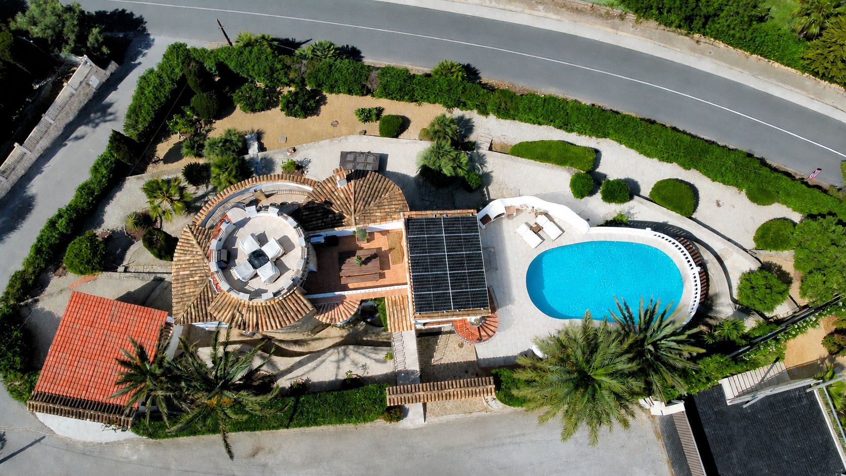 Vista aérea de la villa, destacando la piscina ovalada, los paneles solares y la terraza circular en la azotea con mobiliario exterior.