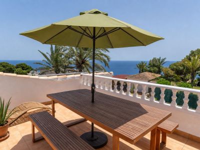 Amplia terraza en la azotea con mesa y bancos de madera, sombrilla verde y vistas panorámicas al mar Mediterráneo, enmarcada por una balaustrada blanca.