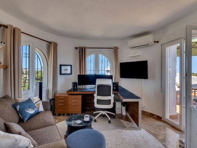 Despacho luminoso con escritorio en L, ventanas arqueadas con rejas y vistas al exterior, complementado por un sofá y acceso directo a la terraza.