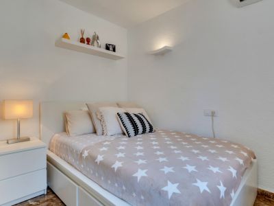 Dormitorio individual con cama moderna, couette de estrellas, mesita de noche blanca y estante decorativo. Iluminación mural y suelo de mármol.
