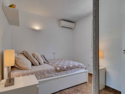 Dormitorio secundario con paredes blancas texturizadas, cama con edredón de estrellas y mesita de noche con lámpara moderna. Incluye aire acondicionado y suelo de baldosas.