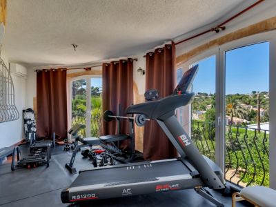 Gimnasio en casa equipado con cinta de correr y pesas, ofreciendo vistas panorámicas a la vegetación y al paisaje desde sus grandes ventanales.