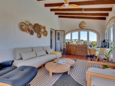 Luminosa terraza acristalada con vigas de madera vistas, suelos de terracota y ventanas arqueadas que ofrecen vistas al paisaje. Integra zona de estar y escritorio.