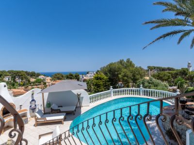 Piscina curva con terraza de azulejos, zona de barbacoa tradicional y vistas panorámicas al mar Mediterráneo y al faro.
