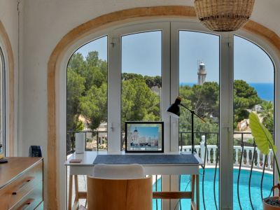 Rincón de trabajo luminoso con vistas panorámicas al mar, el faro y la piscina, enmarcado por un arco de piedra.