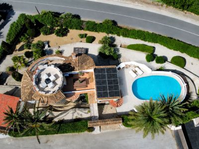 Vista aérea de la villa, destacando la piscina ovalada, los paneles solares y la terraza circular en la azotea con mobiliario exterior.