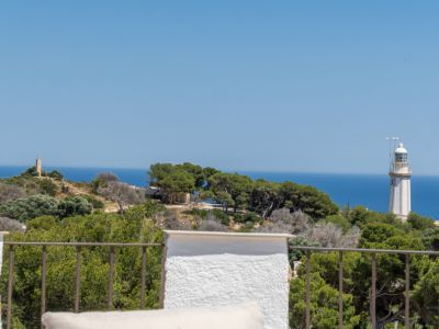 Vista panorámica desde la terraza con barandilla de metal, mostrando el mar Mediterráneo, el faro y una torre de piedra en la distancia.