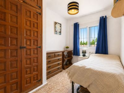 Este acogedor dormitorio presenta un armario empotrado de madera con paneles decorativos y herrajes negros tradicionales. La luz natural entra por una ventana con cortinas azules y vistas a la vegetación.