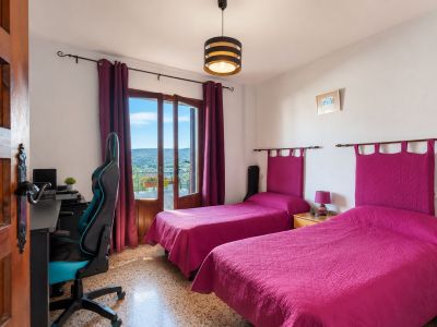 Luminoso dormitorio con dos camas individuales, cabeceros fucsia y acceso directo a balcón con vistas a las montañas. Incluye zona de escritorio y suelo de terrazo.
