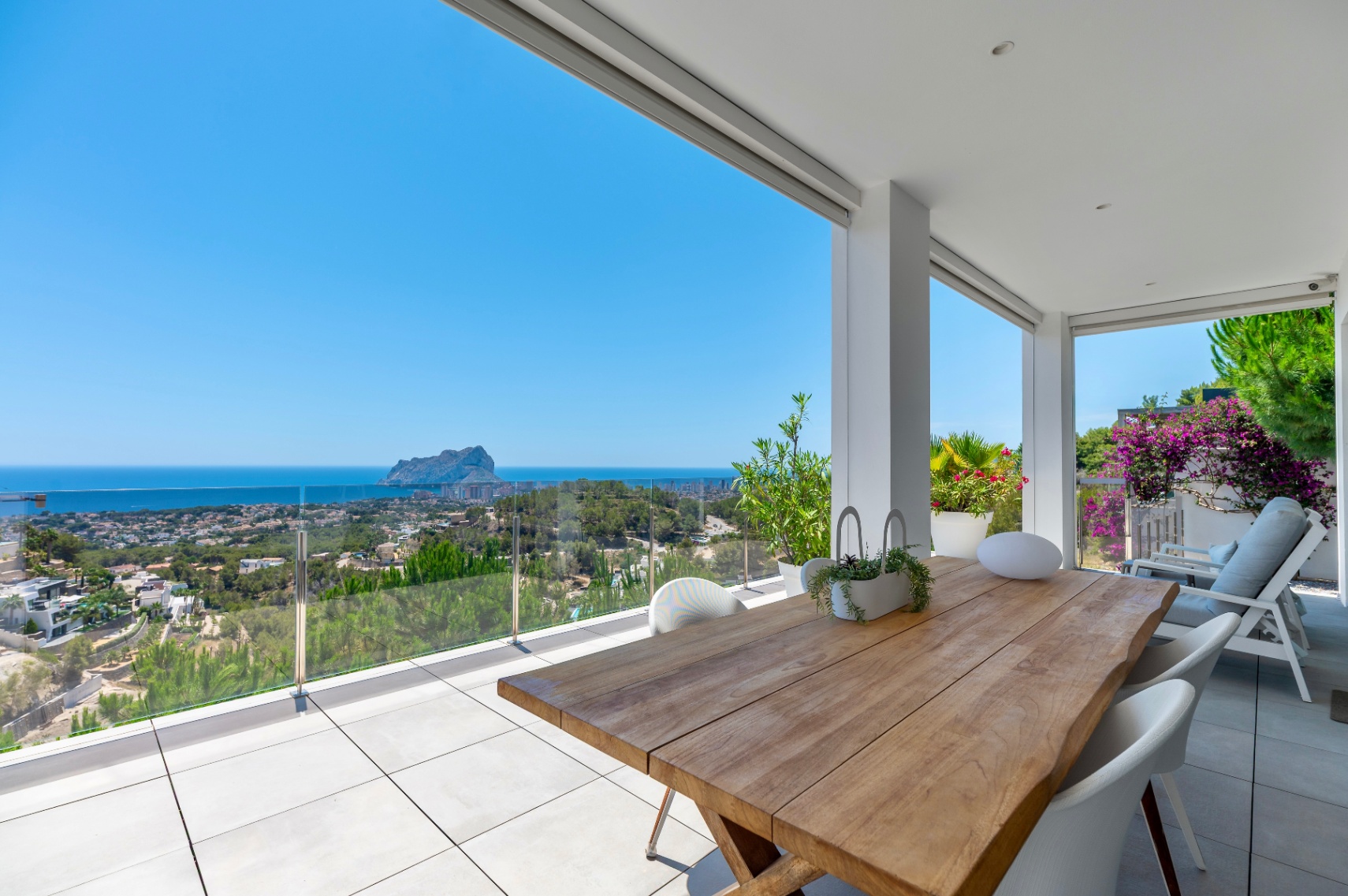 Amplia terraza cubierta con mesa de comedor de madera maciza y sillas blancas. Ofrece vistas panorámicas al mar, Calpe y el Peñón de Ifach a través de barandilla de cristal. Amplia terraza cubierta con mesa de comedor de madera maciza y sillas blancas. Ofrece vistas panorámicas al mar, Calpe y el Peñón de Ifach a través de barandilla de cristal.