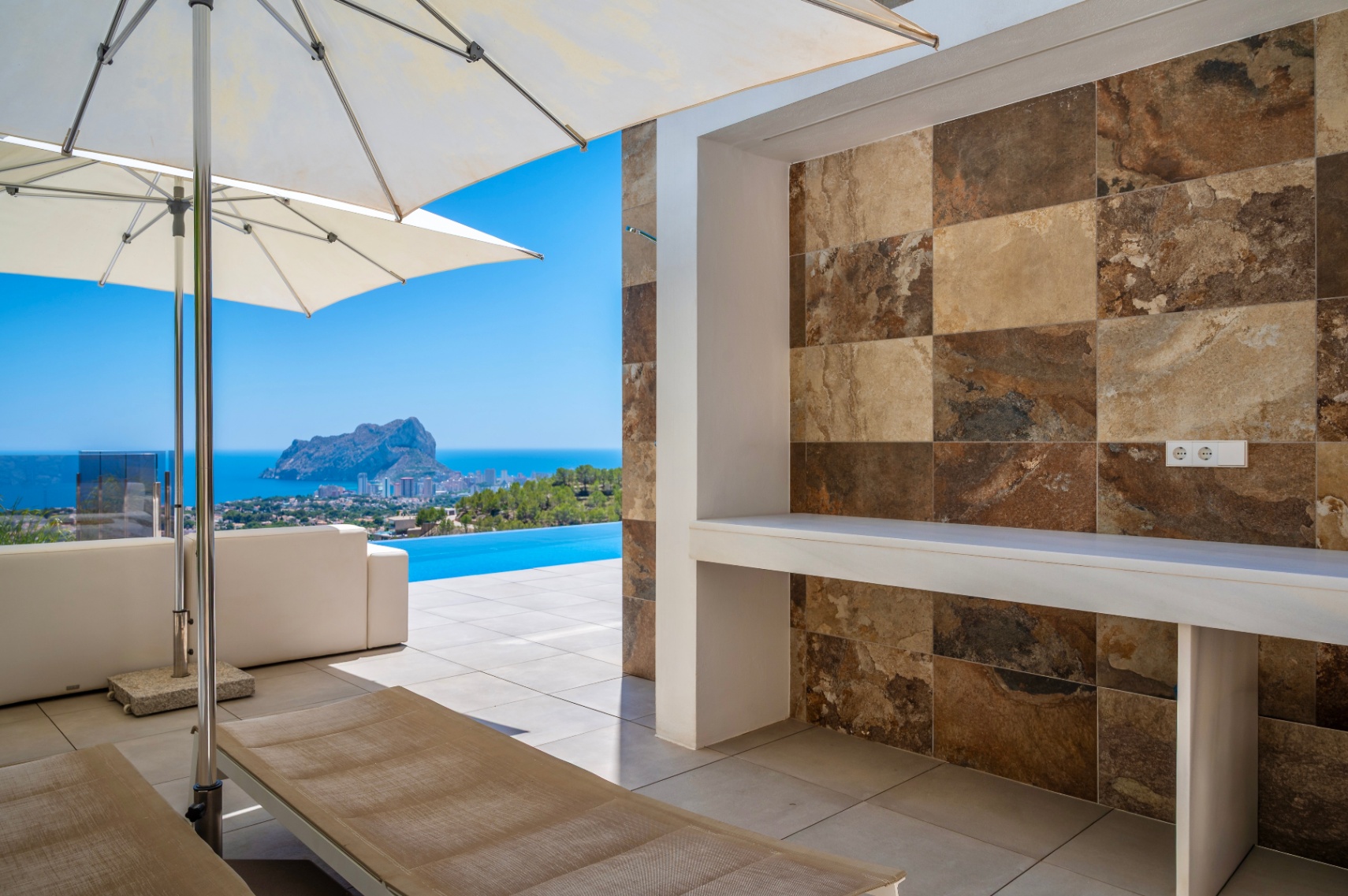 Amplia terraza exterior con mostrador integrado de azulejos efecto piedra natural en tonos variados. Vistas panorámicas al mar, piscina infinita y el Peñon de Ifach. Amplia terraza exterior con mostrador integrado de azulejos efecto piedra natural en tonos variados. Vistas panorámicas al mar, piscina infinita y el Peñon de Ifach.