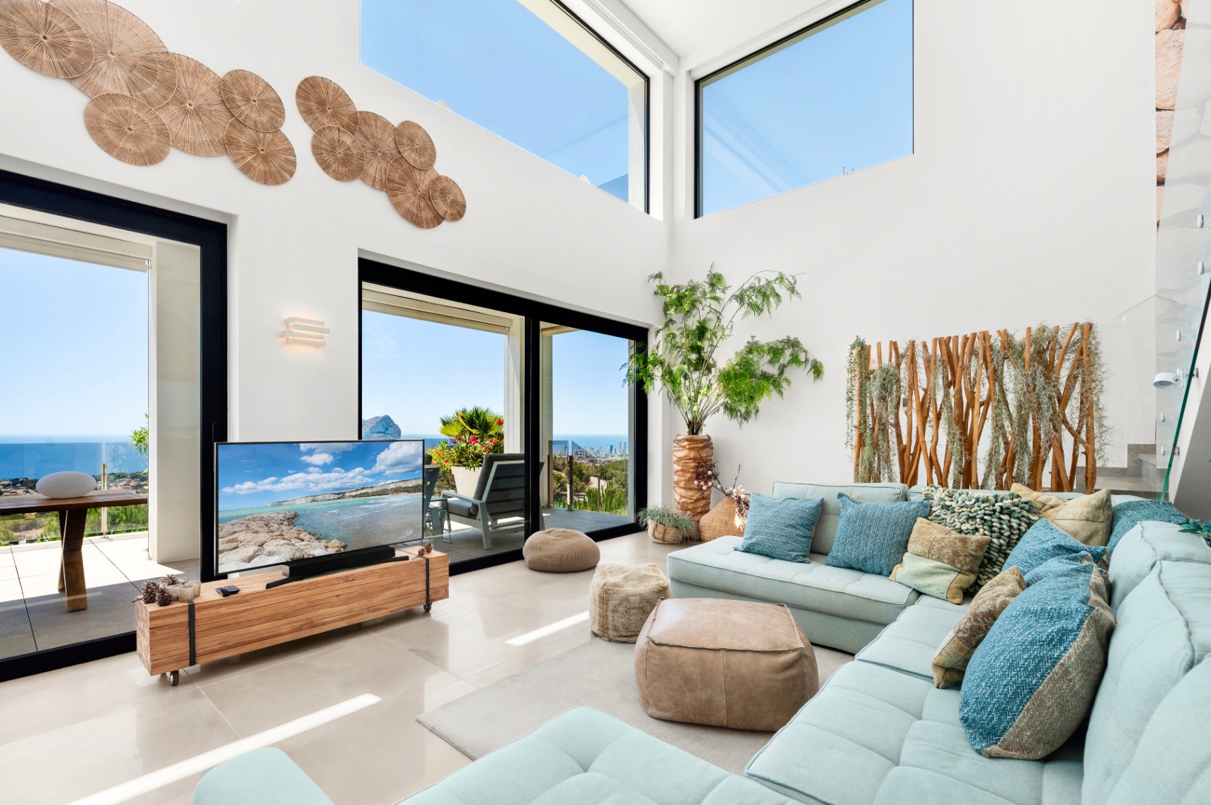 Amplio salón con techos altos, grandes ventanales y puertas correderas que ofrecen vistas panorámicas al mar. Un sofá seccional azul claro se combina con detalles de madera y arte mural. Amplio salón con techos altos, grandes ventanales y puertas correderas que ofrecen vistas panorámicas al mar. Un sofá seccional azul claro se combina con detalles de madera y arte mural.