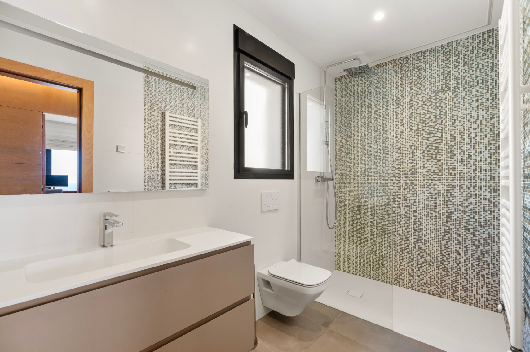 Baño moderno con ducha a ras de suelo y pared de mosaico en tonos tierra. Incluye un mueble de lavabo flotante con lavamanos integrado, inodoro suspendido y ventana con marco negro. Baño moderno con ducha a ras de suelo y pared de mosaico en tonos tierra. Incluye un mueble de lavabo flotante con lavamanos integrado, inodoro suspendido y ventana con marco negro.
