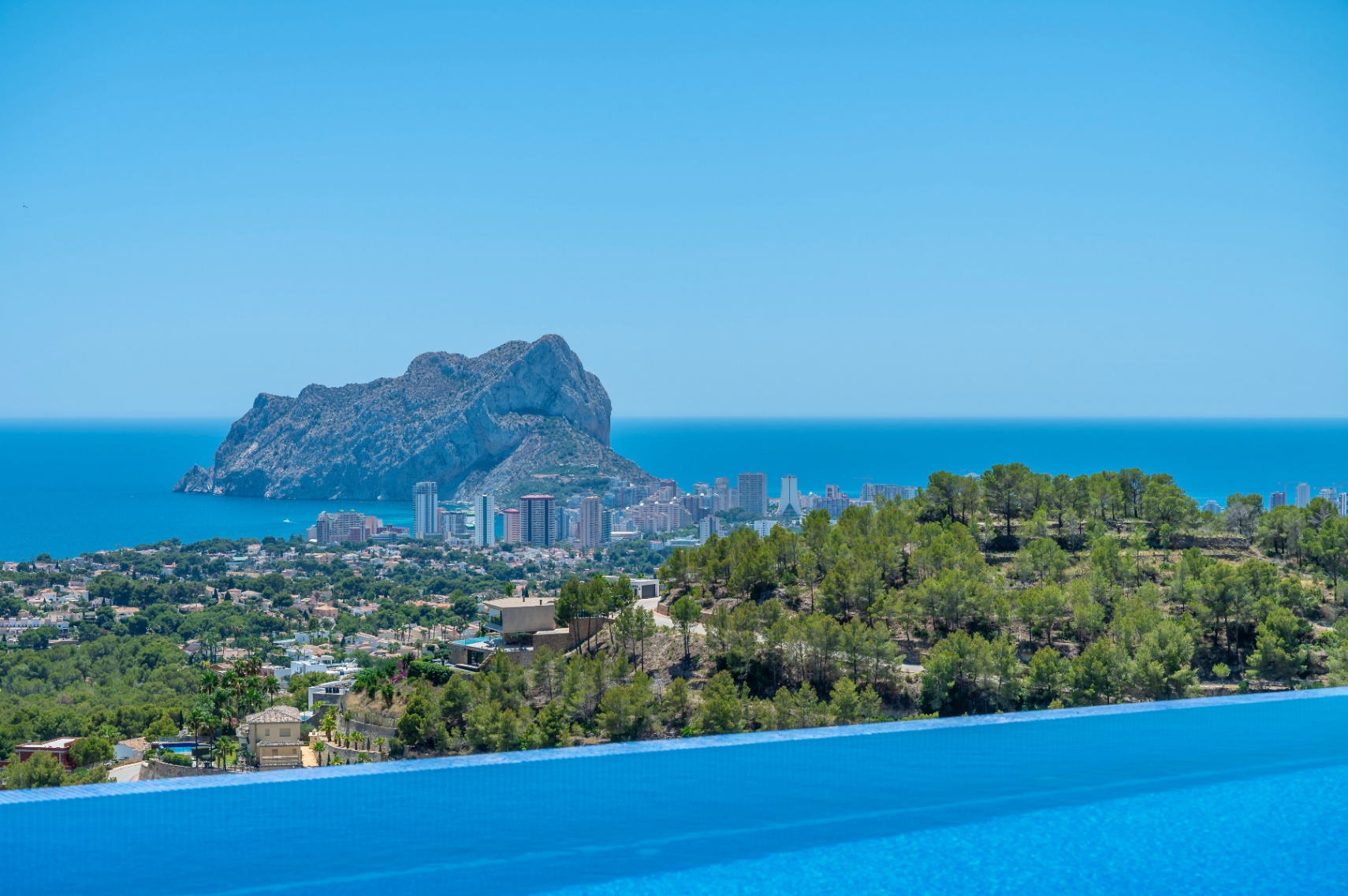 Borde de piscina infinita con vistas panorámicas al Mediterráneo, la ciudad de Calpe y el imponente Peñón de Ifach. Borde de piscina infinita con vistas panorámicas al Mediterráneo, la ciudad de Calpe y el imponente Peñón de Ifach.