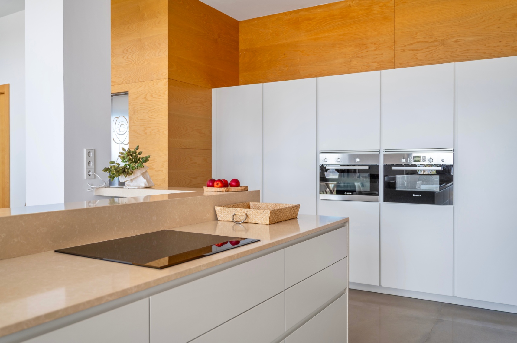 Cocina moderna con encimera color arena e inducción integrada. Destacan los hornos Bosch empotrados y un panel decorativo de madera clara. Cocina moderna con encimera color arena e inducción integrada. Destacan los hornos Bosch empotrados y un panel decorativo de madera clara.