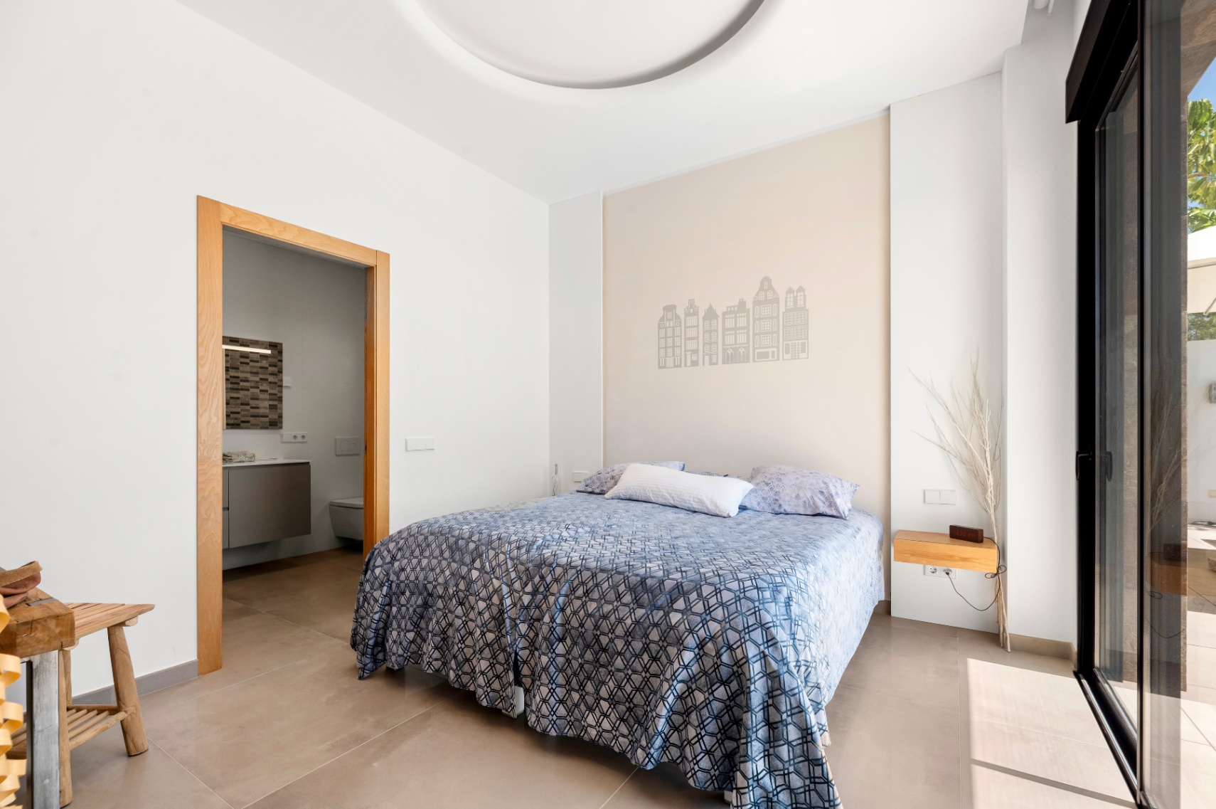 Dormitorio luminoso con cama doble y cabecero decorado con siluetas de edificios. Cuenta con acceso a un baño en suite y salida directa a la terraza a través de una puerta corredera de cristal. Dormitorio luminoso con cama doble y cabecero decorado con siluetas de edificios. Cuenta con acceso a un baño en suite y salida directa a la terraza a través de una puerta corredera de cristal.