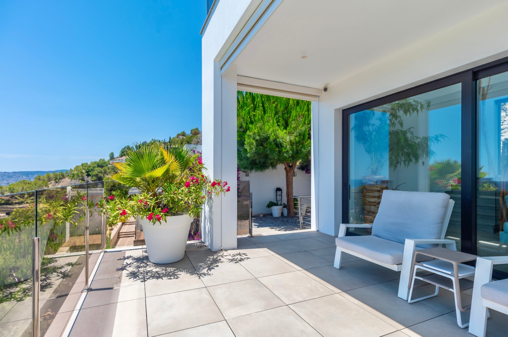 Moderna terraza exterior con suelo de baldosas grises claras y barandilla de cristal, ofreciendo vistas despejadas a la ladera verde. Incluye asientos cómodos y plantas en maceta bajo luz natural. Moderna terraza exterior con suelo de baldosas grises claras y barandilla de cristal, ofreciendo vistas despejadas a la ladera verde. Incluye asientos cómodos y plantas en maceta bajo luz natural.