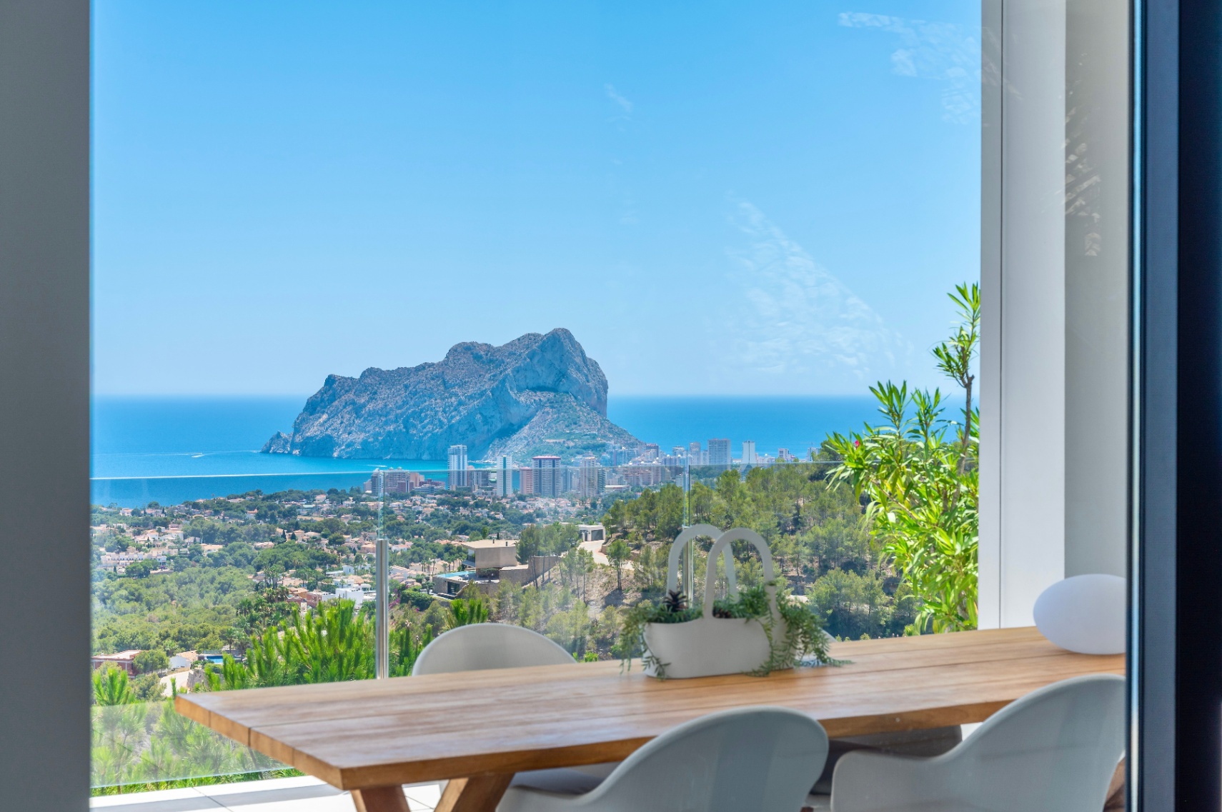 Terraza comedor exterior con mesa de madera y sillas blancas, enmarcando vistas panorámicas del Peñon de Ifach, el mar Mediterráneo y la costa de Calpe. Terraza comedor exterior con mesa de madera y sillas blancas, enmarcando vistas panorámicas del Peñon de Ifach, el mar Mediterráneo y la costa de Calpe.