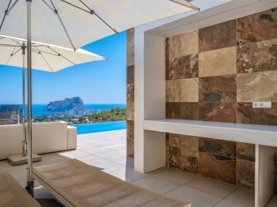 Amplia terraza exterior con mostrador integrado de azulejos efecto piedra natural en tonos variados. Vistas panorámicas al mar, piscina infinita y el Peñon de Ifach.