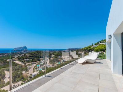 Amplia terraza exterior con suelo de baldosas claras, una moderna tumbona blanca y barandilla de cristal. Vistas panorámicas al mar Mediterráneo, el Peñón de Ifach y la costa de Calpe.