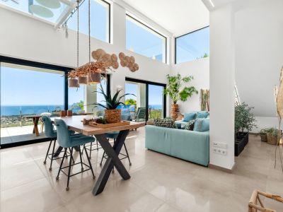 Amplio salón-comedor de planta abierta con techos altos, grandes ventanales y una lámpara de ramas única. Disfrute de vistas panorámicas al mar, la costa y el Peñón de Ifach desde este luminoso interior.