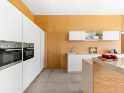 Cocina moderna con armarios blancos integrados y hornos Bosch. Destaca la isla central con encimera de piedra clara y el revestimiento de madera clara en paredes y techo.