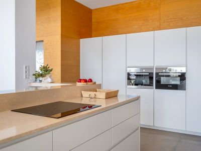 Cocina moderna con encimera color arena e inducción integrada. Destacan los hornos Bosch empotrados y un panel decorativo de madera clara.