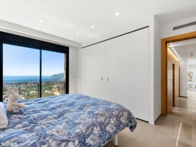 Dormitorio con puertas correderas de cristal de suelo a techo ofreciendo vistas panorámicas al mar y la ciudad. Incluye armarios empotrados blancos y suelo porcelánico claro.