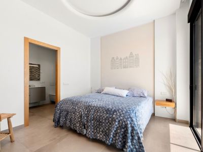 Dormitorio luminoso con cama doble y cabecero decorado con siluetas de edificios. Cuenta con acceso a un baño en suite y salida directa a la terraza a través de una puerta corredera de cristal.