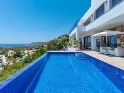 Piscina infinita de mosaico azul con escalones integrados, flanqueada por una amplia terraza con mobiliario lounge y vistas panorámicas a la costa y la ciudad.