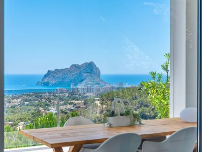 Terraza comedor exterior con mesa de madera y sillas blancas, enmarcando vistas panorámicas del Peñon de Ifach, el mar Mediterráneo y la costa de Calpe.