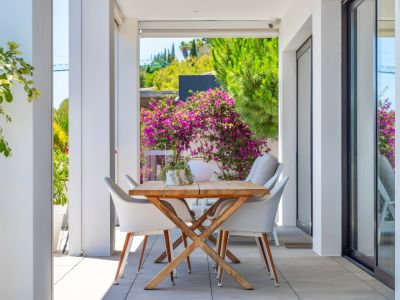 Terraza cubierta con mesa de comedor de madera y sillas blancas, enmarcada por exuberante vegetación y vibrantes buganvillas, ideal para comidas al aire libre.