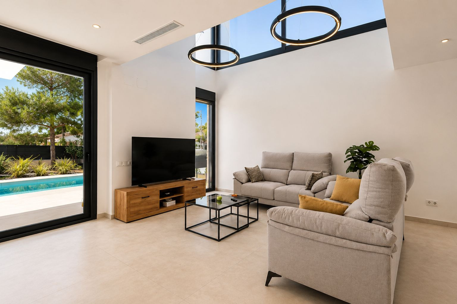 Amplio salón con techo de doble altura, lucernarios y modernas lámparas circulares. Una gran puerta de cristal conecta con la piscina privada y el jardín, maximizando la luz natural.