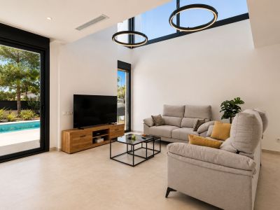Amplio salón con techo de doble altura, lucernarios y modernas lámparas circulares. Una gran puerta de cristal conecta con la piscina privada y el jardín, maximizando la luz natural.