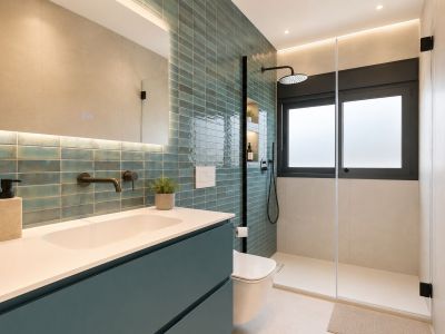 Baño moderno con pared de azulejos turquesa, grifería negra empotrada y amplia ducha con mampara de cristal, ventana esmerilada y nichos iluminados.
