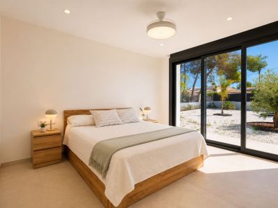 Dormitorio con cama de madera, mesitas a juego y acceso directo a un jardín de grava a través de amplias puertas correderas de cristal. Iluminación empotrada y ventilador de techo.
