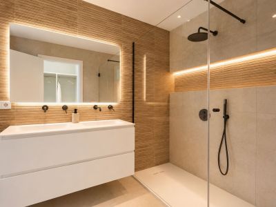 Moderno baño con doble lavabo flotante, grifería negra y espejo retroiluminado. Ducha a ras de suelo con mampara de cristal y azulejos texturizados en madera.