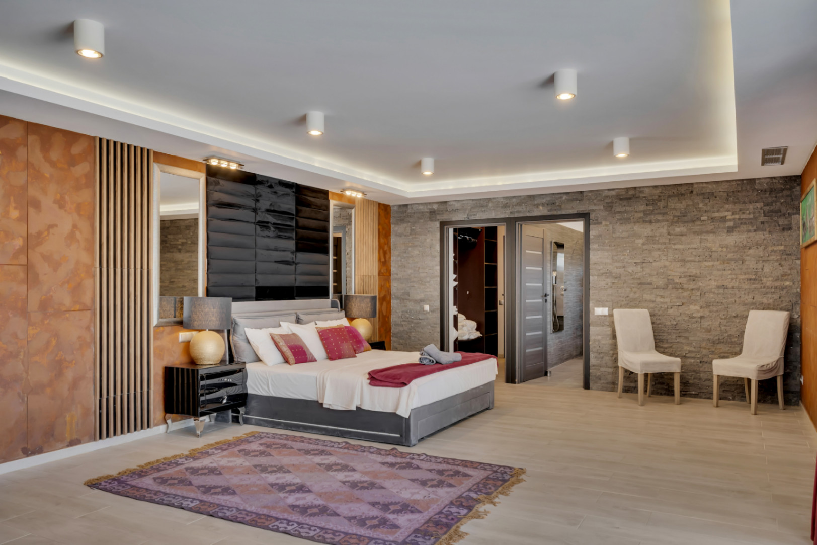 Amplio dormitorio con diseño moderno, pared de efecto piedra, cabecero acolchado y luces LED integradas. Acceso directo a vestidor y baño en suite para mayor confort.