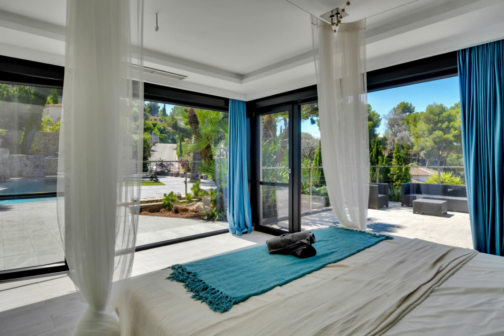 Dormitorio luminoso con acceso directo a una amplia terraza exterior, piscina y vistas a la vegetación a través de grandes ventanales de suelo a techo.
