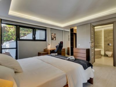 Amplio dormitorio con cama doble, escritorio de madera y ventanales que dan al exterior. Incluye armario con espejo, cómoda y acceso directo a un baño en suite con azulejos contemporáneos.