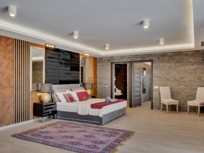 Amplio dormitorio con diseño moderno, pared de efecto piedra, cabecero acolchado y luces LED integradas. Acceso directo a vestidor y baño en suite para mayor confort.