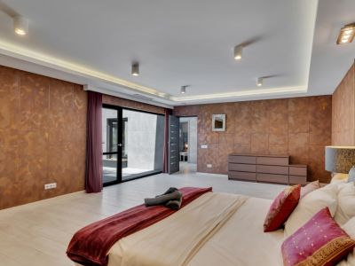 Amplio dormitorio con paredes de acabado cobrizo texturizado y suelo claro. Dispone de acceso directo a un patio exterior a través de una gran puerta corredera de cristal y una iluminación de techo moderna.