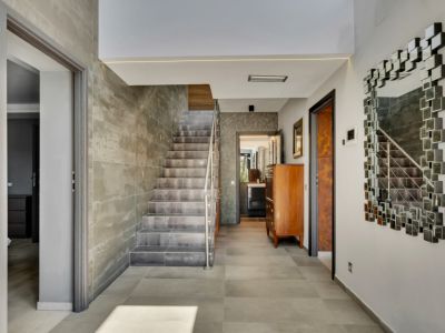 Amplio recibidor con escalera de diseño, revestida con azulejos de efecto hormigón y barandilla de acero inoxidable. El suelo es de gres porcelánico gris y un espejo modular decora la pared.