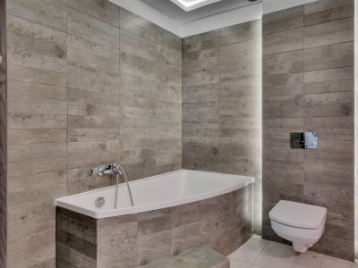 Baño moderno con bañera integrada y WC suspendido, destacando los revestimientos cerámicos grises con textura de madera y la iluminación LED vertical integrada.